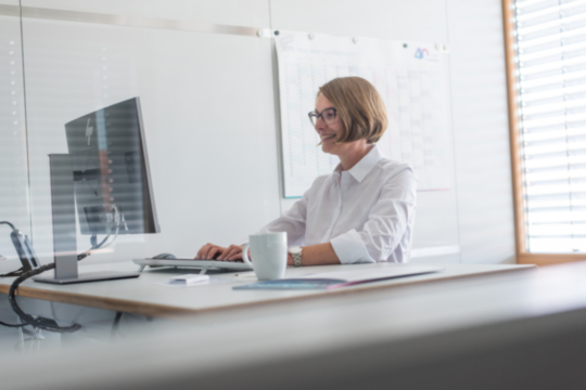 Zeigt eine fröhliche Dame, die mit dem Online-Schulungssystem am PC arbeitet.